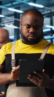 Dikey video endüstrisi 4.0 fotovoltaik fabrika mühendisi güneş pillerinin enerji üretimini maksimuma çıkarmak için tablet üzerinde yazılım kullanıyor. Güneş panellerini denetleyen Afrikalı Amerikalı adam akıllı fabrika.