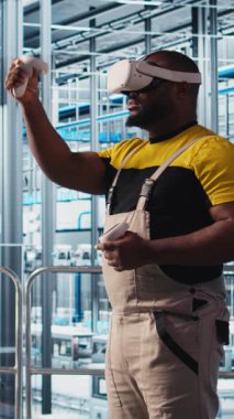 Sanayi 4.0 güneş paneli fabrikasında sanal gerçeklik teknolojisi kullanan dikey video mühendisi yenilenebilir enerji üretiyor. Fotovoltaik teknisyeni. Akıllı fabrika. VR kulaklık ve kamera A kullanarak veri analiz ediyor.