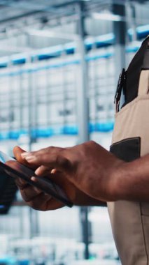 Dikey video akıllı fabrika uzmanı otomatik sistemleri test etmek ve güvenilirliği sağlamak için dijital cihaz uygulaması kullanıyor. İşçi, algılayıcı verilerine dayanarak darboğazları belirlemek ve ekipmanları optimize etmek için tablet kullanır