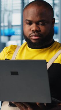 Dikey video mühendisi 4.0 endüstriyel sanayi tesisinde dizüstü bilgisayar kullanarak makine kuruyor ve kapsamlı testler yapıyor. Akıllı fabrika kalibrasyonunda not defteri kullanan neşeli robot teknisyeni.