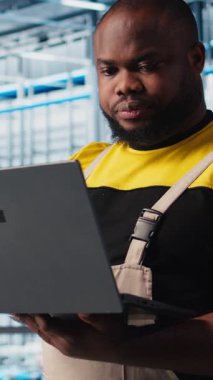 Dikey video endüstrisi 4.0 endüstriyel fabrika mühendisi robot makineleri yapay zeka teknolojisi kullanarak otomatikleştiriyor. Afro-Amerikalı adam akıllı fabrikada yapay zeka özelliklerini not defteri ve kamera A kullanarak uyguluyor.