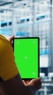 Otomatik sistemleri test etmek ve güvenilirliği sağlamak için yeşil ekran tableti kullanan dikey video akıllı fabrika uzmanı. İşçi, dar boğazları tanımlamak ve sensörlere dayalı donanımı optimize etmek için krom anahtar aygıtı kullanır