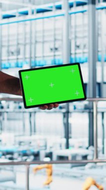 Dikey video akıllı fabrika mühendisi, yeşil ekran tablet kullanan robotik silah ve taşıma bantlarının çalışmasını denetliyor. Sektör 4.0 bitki teknisyeni krom anahtar aygıtı kullanılarak sistem performansını izler