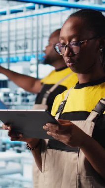 Dikey video endüstrisi 4.0 bitki teknisyeni dijital cihaz uygulaması kullanılarak sistem performansını gözlemler. Akıllı fabrika mühendisi, tablet üzerindeki yazılımı kullanarak robotik silah ve taşıma bantlarının çalışmasını denetliyor.