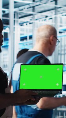 Dikey video mühendisi, makineleri yüklemek için 4.0 endüstriyel fabrikada yeşil ekran dizüstü bilgisayar kullanıyor. Robot teknisyenleri akıllı fabrika sensörlerini ayarlayan, sensörleri çalıştıran...