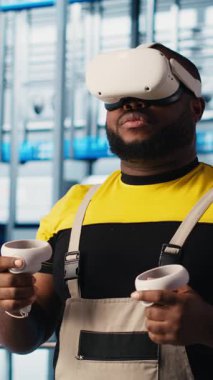 Dikey video akıllı fabrika mühendisi robotik silah ve taşıma bantlarının çalışmasını denetlemek için VR kulaklık kullanıyor. Sanayi 4.0 bitki teknisyeni sanal gerçeklik ve kamera kullanarak sistem performansını izler