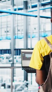 Akıllı fabrikada dizüstü bilgisayar kullanan dikey video çalışanı veri toplayıp analiz ediyor. Gelişmiş sensörlerle donatılmış 4.0 endüstriyel fabrikada izleme yazılımı kullanan Afrikalı Amerikalı bir kadın.