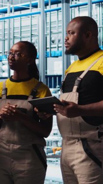 Dikey video Photovoltaics akıllı fabrika mühendisi gerekli ayarlamaları not alıyor, iş arkadaşlarıyla konuşuyor. Endüstri 4.0 güneş panelleri fabrika ekip lideri üretim planlarını değiştiriyor, kamera A