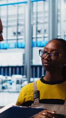 Dikey video Photovoltaics akıllı fabrika mühendisi gerekli ayarlamaları not alıyor, iş arkadaşlarıyla konuşuyor. Endüstri 4.0 güneş panelleri fabrika ekip lideri üretim planlarını değiştiriyor, kamera A