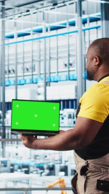 Dikey video akıllı fabrika uzmanı otomatik sistemleri test etmek ve güvenilirliği sağlamak için dizüstü bilgisayar kullanıyor. Kadın dar geçitleri tanımlamak ve ekipmanları ve kamerayı optimize etmek için izole ekran defteri kullanır