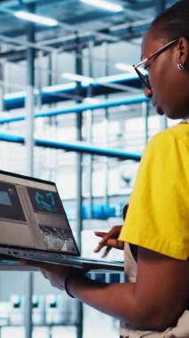 Dikey video akıllı fotovoltaik fabrika uzmanı dizüstü bilgisayardaki sistem performans ölçümlerine bakıyor. Afrika Amerika güneş panelleri fabrika işçisi IoT sensörleri aracılığıyla enerji üretimini izliyor