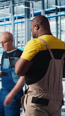 Dikey video endüstrisi 4.0 endüstriyel fabrika uzmanı tablet üzerindeki CAD programını kullanarak yeni robot makineler tasarlıyor. Afrika kökenli Amerikalı bir adam akıllı fabrikada otomasyon ekipmanları için cihaz kullanıyor.