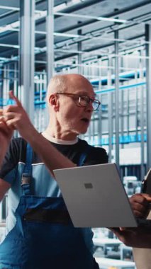 Dikey video Photovoltaics akıllı fabrika lideri stajyere bilgisayarla hasarlı IOT sensörlerini nasıl tamir edeceğini öğretiyor. Sanayi 4.0 güneş panelleri. Bitki, stajyer mühendisleri azaltma konusunda deneyimli.