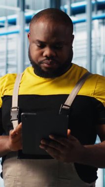 Dikey video Photovoltaics akıllı fabrika uzmanı tablet kullanarak verileri analiz ediyor. Endüstrideki Afrikalı Amerikalı adam 4.0 güneş paneli fabrika yenilenebilir enerji üretiyor sistemi incelemek için defter kullanıyor