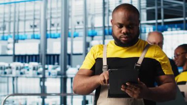 Akıllı fabrika mühendisi tesis katındaki robot silah ve montaj hatlarını denetliyor. Endüstri 4.0 Afro-Amerikan erkeği sistem performansını izliyor ve sorun yaratıyor, kamera A