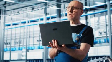 Yaşlı mühendis, otomatik sistemleri test etmek ve güvenilirliği sağlamak için akıllı fabrikada dizüstü bilgisayar kullanır. Deneyimli teknisyen, darboğazları tanımlamak ve ekipmanları optimize etmek için A kamerasını kullanır.