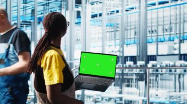 Akıllı bir fabrika teknisyeni robot kolları kontrol ediyor. Model defter kullanarak, kapat. Sektör 4.0 endüstriyel santraldeki mühendis otomatik makineleri yeşil ekran dizüstü bilgisayar ve kamera A kullanarak kontrol ediyor.