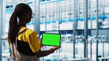 Akıllı fabrika uzmanı otomatik sistemleri test etmek ve güvenilirliği sağlamak için model dizüstü bilgisayar kullanıyor. Kadın darboğazları tanımlamak ve ekipmanları optimize etmek için izole ekran defteri kullanır, kamera A