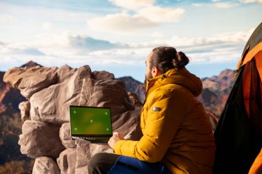 Macera Avcısı, izole edilmiş krom anahtarın yanındaki dağın zirvesinde duruyor ve önünde durmaksızın uzanan manzara manzarasına bakıyor. Temiz hava ve nefes kesici manzara..