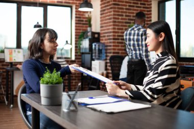 Beyaz bir kadın, tuğla duvar çalışma alanındaki bir röportajda CV 'sini kadın işe alıcıya verdi. Asyalı İK yöneticisi iş başvurusu için adaydan başvuru formu aldı ve istihdam toplantısına başladı.