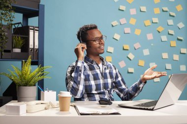 Tele pazarlamacı masada oturuyor ve başvuru belgeleri için bir müşteriye telefonda yardım ediyor. Şirket danışmanı laptopunu kullanıyor ve bir telefon görüşmesi yapıyor, çalışana yardım sağlıyor..