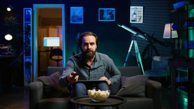 Neon ışıklı dairede dizüstü bilgisayar kullanarak TV 'de şok edici bir son dakika haberi izleyen adam. Televizyonun sesini açan kişi, dizüstü bilgisayar ve B kamerasıyla koltukta otururken yaşanan olaylara şaşırdı.