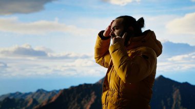 Trekker yüksek rakımlı manzaranın tadını çıkarıyor ve bir telefon görüşmesi yapıyor, panoramik dağ manzarası ve gevşek hava rahatlama için mükemmel bir manzara sağlıyor. Akıllı telefonunda güçlü bir sinyal kullanıyor. Kamera B.