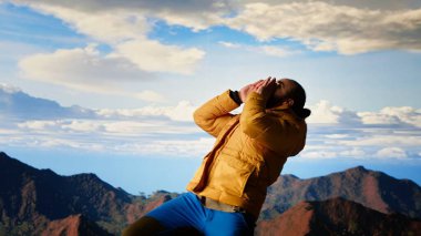 Gezgin yeni zirvelere ulaşıyor ve dağın zirvesinde zafer dansı yapıyor. Tatmin ve motivasyonu hissediyor. Dağların ve gökyüzünün nefes kesici manzarası macerayı yansıtır. Kamera B.