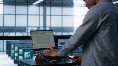 Sunucu odasında bilgisayar bilimci dizüstü bilgisayarda kodlama yapıyor, felaket kurtarma planları geliştiriyor. Veri merkezindeki Afrikalı Amerikalı adam notebook, kamera A kullanarak başarısız senaryoları test ediyor.