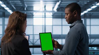 Sunucu odası veri bilimcileri taklit tablet kullanıyor, hataları önlemek için güvenlik denetimleri yapıyor. Veri merkezinde iş arkadaşı olan Afrikalı Amerikalı bir adam yeşil ekran cihazına bakıyor, kamera A