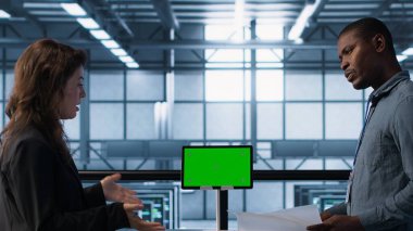 Mühendisler sunucu odasını model cihazıyla denetliyor, donanım belgelerini okuyor. Ekip sunucu merkezinde inceleme yapıyor, yeşil ekran tableti ile ilgili teknik dosyaları okuyor, kamera A