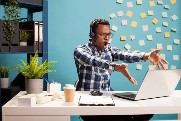 Zenci işadamı, çalışanlarıyla yaptığı hararetli bir telefon görüşmesi sırasında öfkeyle tepki veren bir cihaz ekranını işaret ediyor. Öfkeli finans analisti laptopunda iş arkadaşlarına bağırıyor..