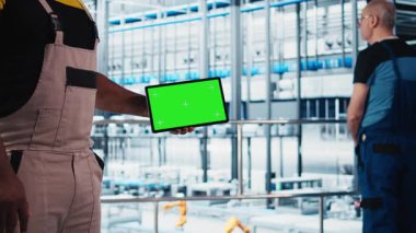 Akıllı fabrika mühendisi, yeşil ekran tablet kullanan robotik silah ve taşıyıcı bantların çalışmasını denetliyor. Endüstri 4.0 bitki teknisyeni renk anahtar aygıtı kullanarak sistem performansını gözlemler, kamera A