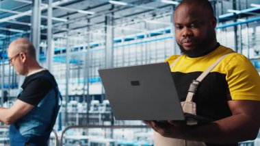 Sanayi 4.0 endüstriyel fabrika mühendisi robot makineleri yapay zeka teknolojisi kullanarak otomatikleştiriyor. Afro-Amerikalı adam akıllı fabrikada yapay zeka özelliklerini not defteri ve kamera A kullanarak uyguluyor.