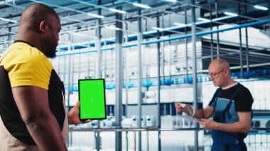 Otomatik sistemleri test etmek ve güvenilirliği sağlamak için yeşil ekran tableti kullanan akıllı bir fabrika uzmanı. İşçi, dar boğazları tanımlamak ve sensör verilerine dayanarak donanımı optimize etmek için krom anahtar aygıtı kullanır, kamera A