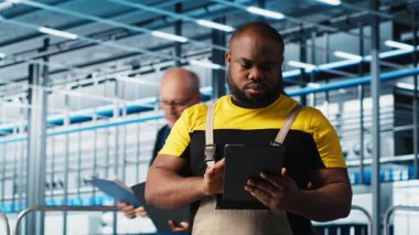 Sanayi 4.0 fotovoltaik fabrikası mühendisi güneş pillerinin enerji üretimini maksimuma çıkarmak için tablet üzerinde yazılım kullanıyor. Güneş panellerini denetleyen Afrikalı Amerikalı adam akıllı fabrika ekipmanları, kamera A