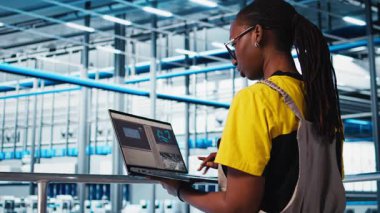 Akıllı fotovoltaik fabrikası uzmanı dizüstü bilgisayardaki sistem performans ölçümlerine bakıyor. Afrika-Amerika güneş panelleri fabrika işçisi IoT sensörleri ve kamera A aracılığıyla enerji üretimini takip ediyor.