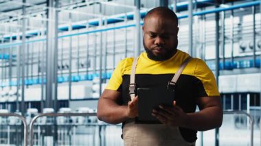 Photovoltaics akıllı fabrika uzmanı tablet kullanarak verileri analiz ediyor. Endüstrideki Afrikalı Amerikalı adam 4.0 güneş panelleri fabrika yenilenebilir enerji üretiyor sistem ölçümlerini gözden geçirmek için defter kullanıyor, kamera A