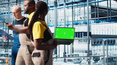 Akıllı fabrika uzmanı otomatik sistemleri test etmek ve güvenilirliği sağlamak için model dizüstü bilgisayar kullanıyor. Kadın darboğazları tanımlamak ve ekipmanları optimize etmek için izole ekran defteri kullanır, kamera A