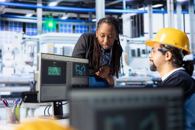 Photovoltaics fabrika denetleyicisi PC 'deki uzman ince ayar sistemi tarafından yapılan işleri denetliyor. Afrika kökenli Amerikalı yönetici güneş panelleri mühendisleri ile birlikte çalışıyor.