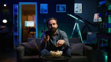 Sıkıcı adam evde kanepede dinleniyor, TV 'de film seyrederken patlamış mısır yiyor. Tembel insan abur cubur yiyor ve RGB 'deki TV kanallarından geçiyor oturma odası, kamera B