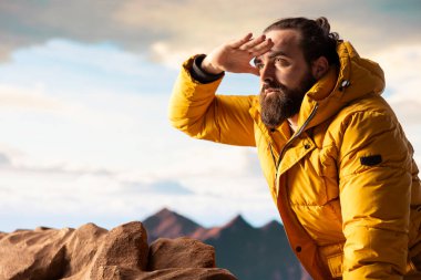 Doğa aşığı nefes kesen bir dağ sırasının kenarında duruyor, yükselen zirvelerin ve uçsuz bucaksız gökyüzünün manzaralı arka planına bakıyor. Genç adam macera ve açık hava keşiflerini seviyor..