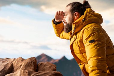 Bir dağ zirvesinde gezgin temiz havayı ve panoramik manzarayı içine çekiyor. Dağcı doğa aşığı engebeli tepelerin, engin gökyüzünün, maceranın ve gezinin çarpıcı manzarasına hayran kalır..