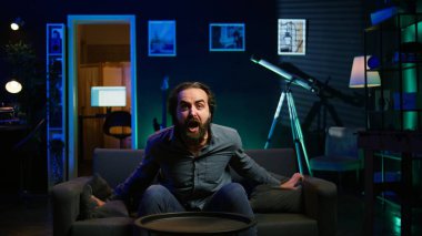 Spor yayınlarını izlerken, taraftarların öfkesinden kudurdu. Yanlışlıkla takımları azarladı. Kızgın adam TV ekranına yastık fırlatırken futbola bakıyor. Fırsatı kaçırdığı için azarlayan oyuncu, kamera B