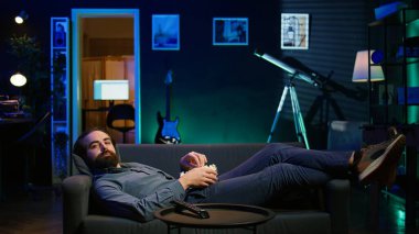 Gülümseyen adam kanepede uzanıp patlamış mısır yerken televizyon kanalında film izleyip tatilin tadını çıkarıyordu. Neşeli insan, apartmanda uzanıp abur cubur yiyor, filmlere bakıyor, B kamerasına bakıyor.