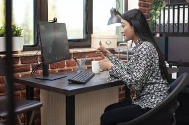 Asyalı girişimci ve erkek müşteri proje gelişimini tartışmak için sanal toplantı konusunda işbirliği yapıyorlar. Ofis masasında bilgisayar başında oturan kadın yönetici, video çağrısında iş arkadaşına iki parmak işareti yapıyor.