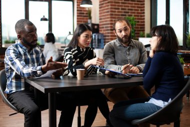Çok ırklı İK ekibi, beyaz kadın adayın mesleki geçmişini değerlendirmek ve sorgulamak için özgeçmişlerini masaya oturttu. Çeşitli acemiler başlangıç ofisinde beyaz bir kadınla röportaj yapıyor.