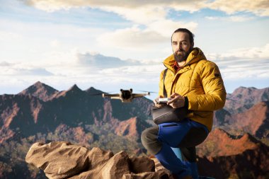 Erkek nüfuzlu kişi, uzaktan kumandayla yüksek kaliteli hava görüntüsü içeriği kaydederek, bir vlog üzerinden yürüyüş yolculuğunu paylaşıyor. Genç yürüyüşçü içerik yaratıcısı manzarayı filme alıyor.