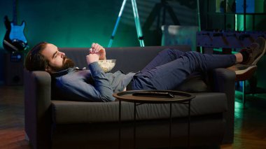 Adam evde oyalanıyor, kanepeye uzanıyor, abur cubur yiyor, televizyon seyrediyor. Sıkıcı bir yaşam tarzı, kanepede uzanmak, televizyon izleyerek zaman harcamak, patlamış mısır yemek, kamera A