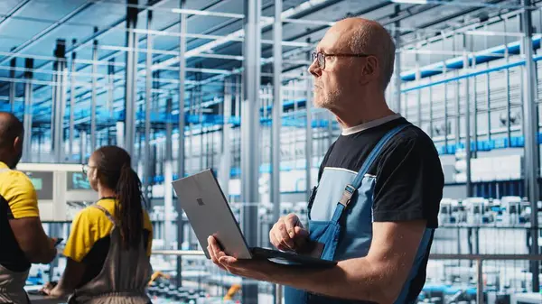 Akıllı fabrika kıdemli mühendisi, robotik silah ve taşıma sistemlerini denetlemek için dizüstü bilgisayar kullanır. Deneyimli sanayi 4.0 bitki teknisyeni sistem performansını not defteri, kamera A kullanarak gözlemliyor.